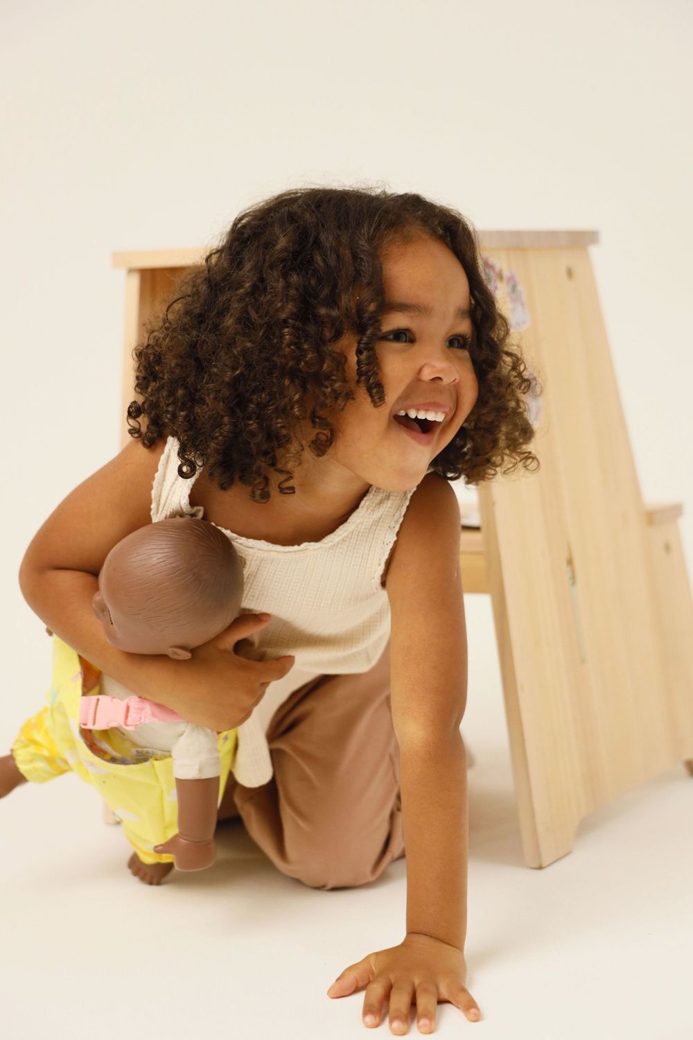 A sequence of photos showing a joyful child crawling and playing on the floor in a white top and brown pants.