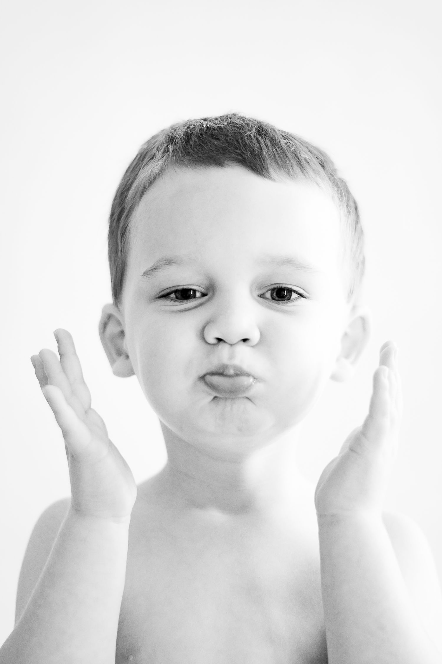 Three high key black and white photos show a child making silly faces and blowing kisses at the camera.