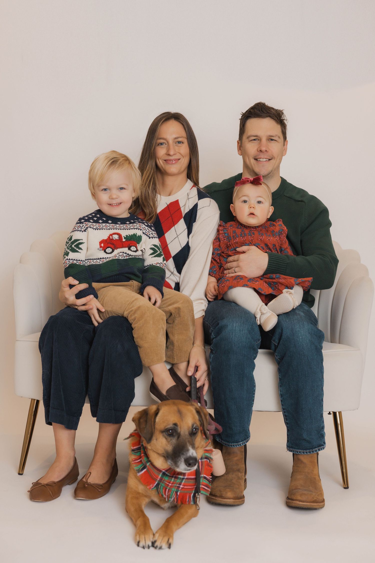 A group sits together on chairs with a brown dog wearing a festive bandana for a holiday photo session.
