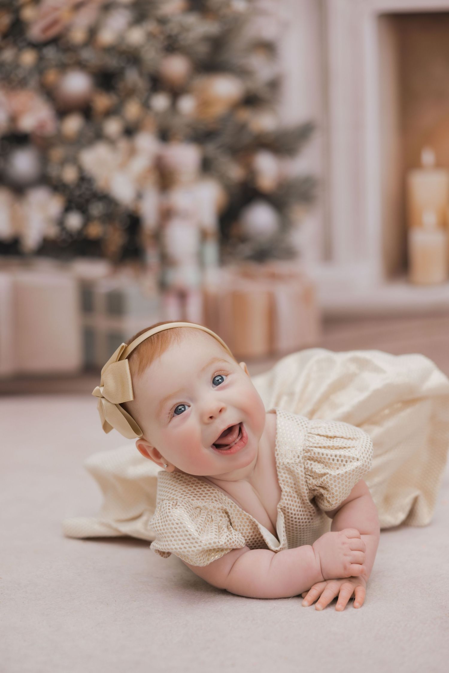 A baby wearing a cream-colored dress lies on a beige carpet while smiling and playing in a sequence of candid shots.