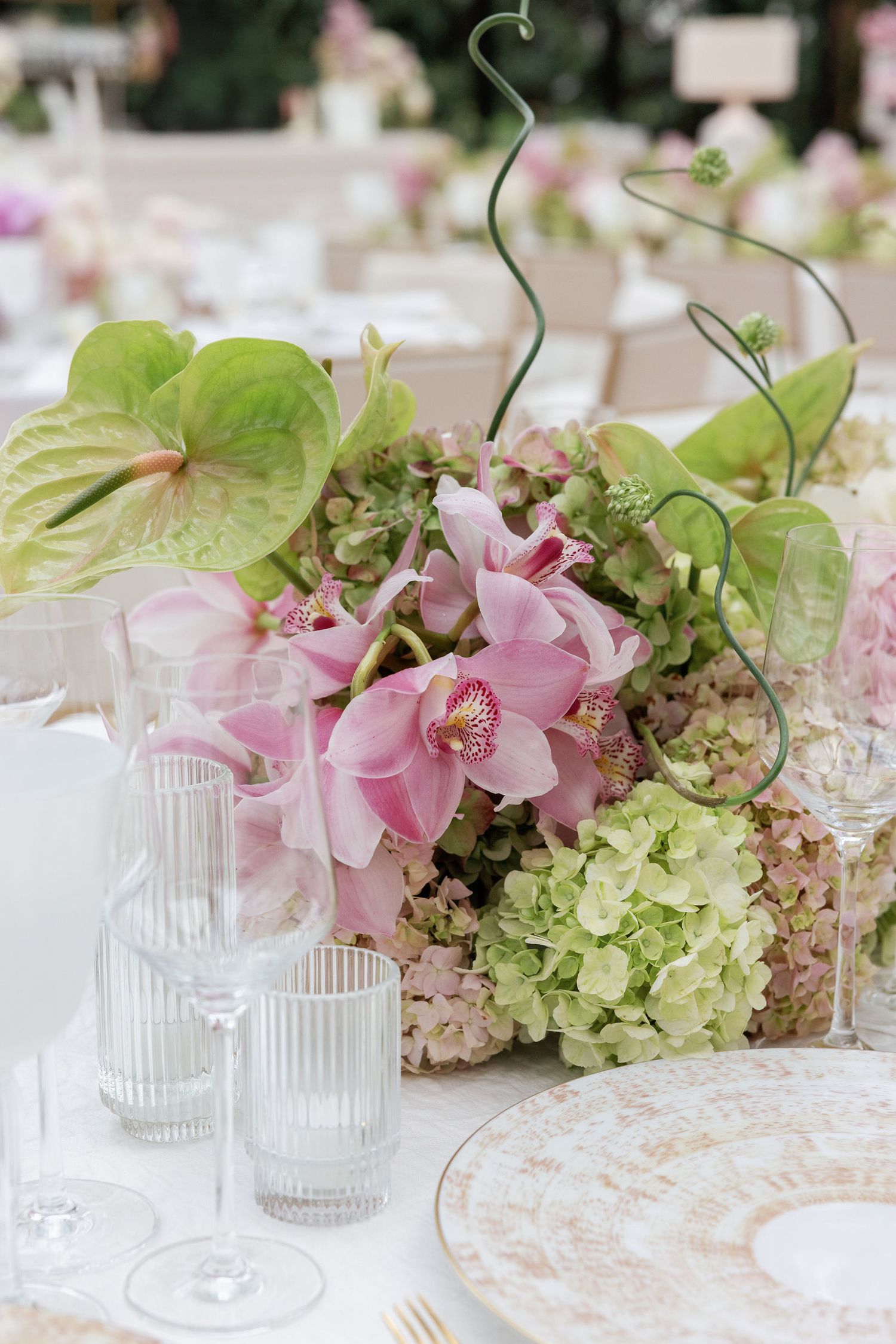 Elegant table setting with pink orchids, green anthurium leaves and hydrangeas in a crystal centerpiece arrangement.
