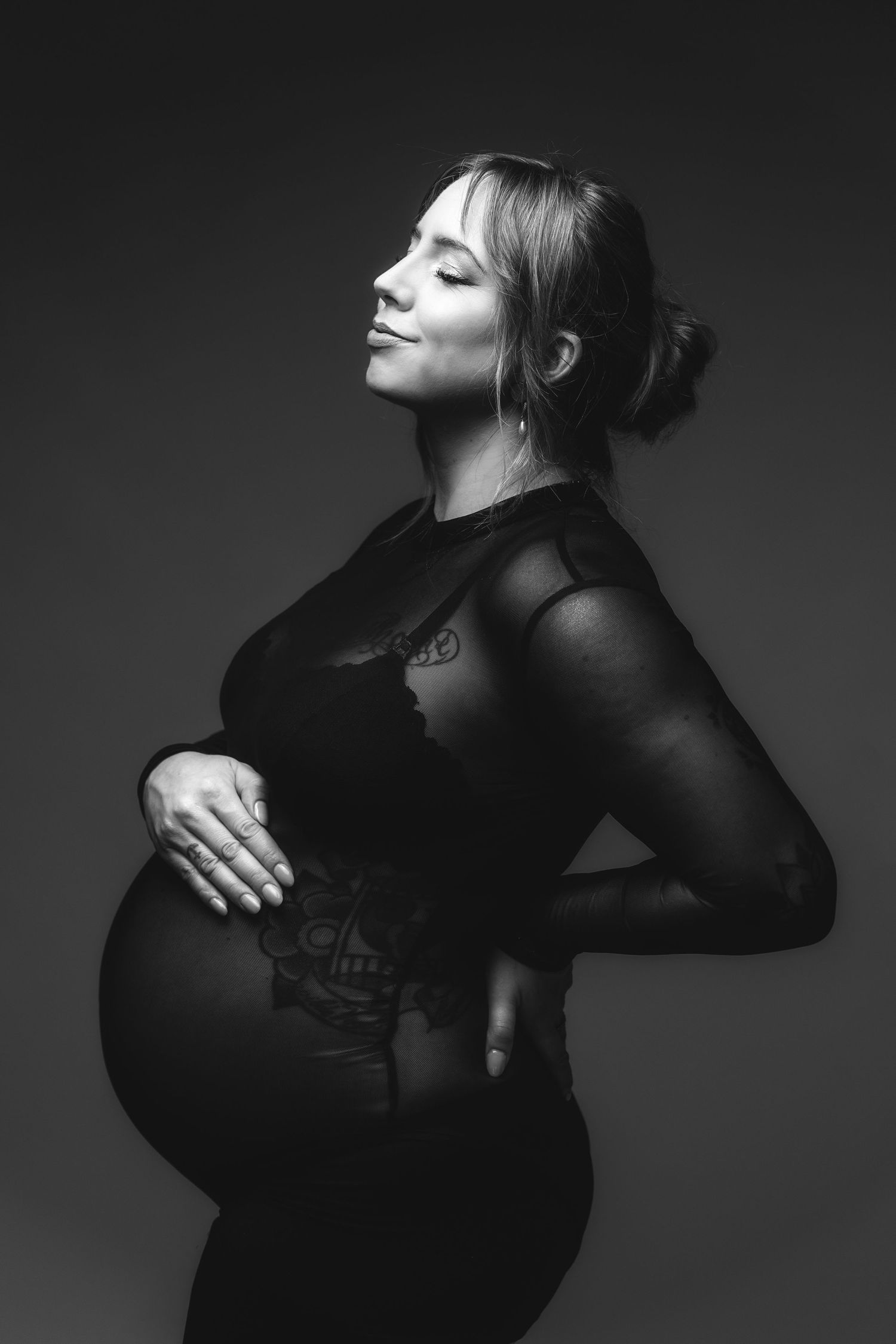 Black and white maternity photography series showing silhouette poses of pregnant woman in dark sheer clothing against dark backdrop.