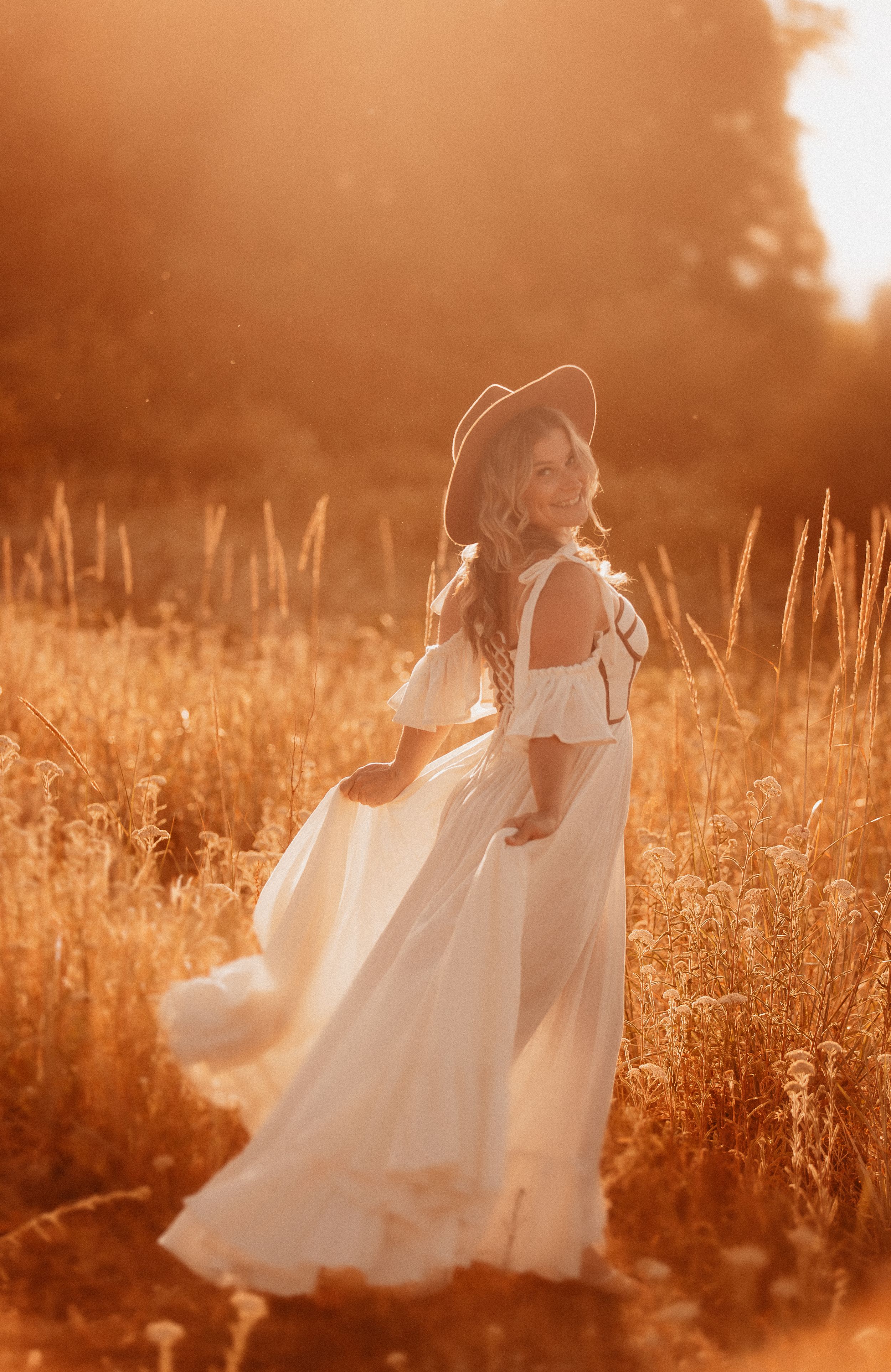 Dreamy sunset maternity session in a golden field with flowing white dress.