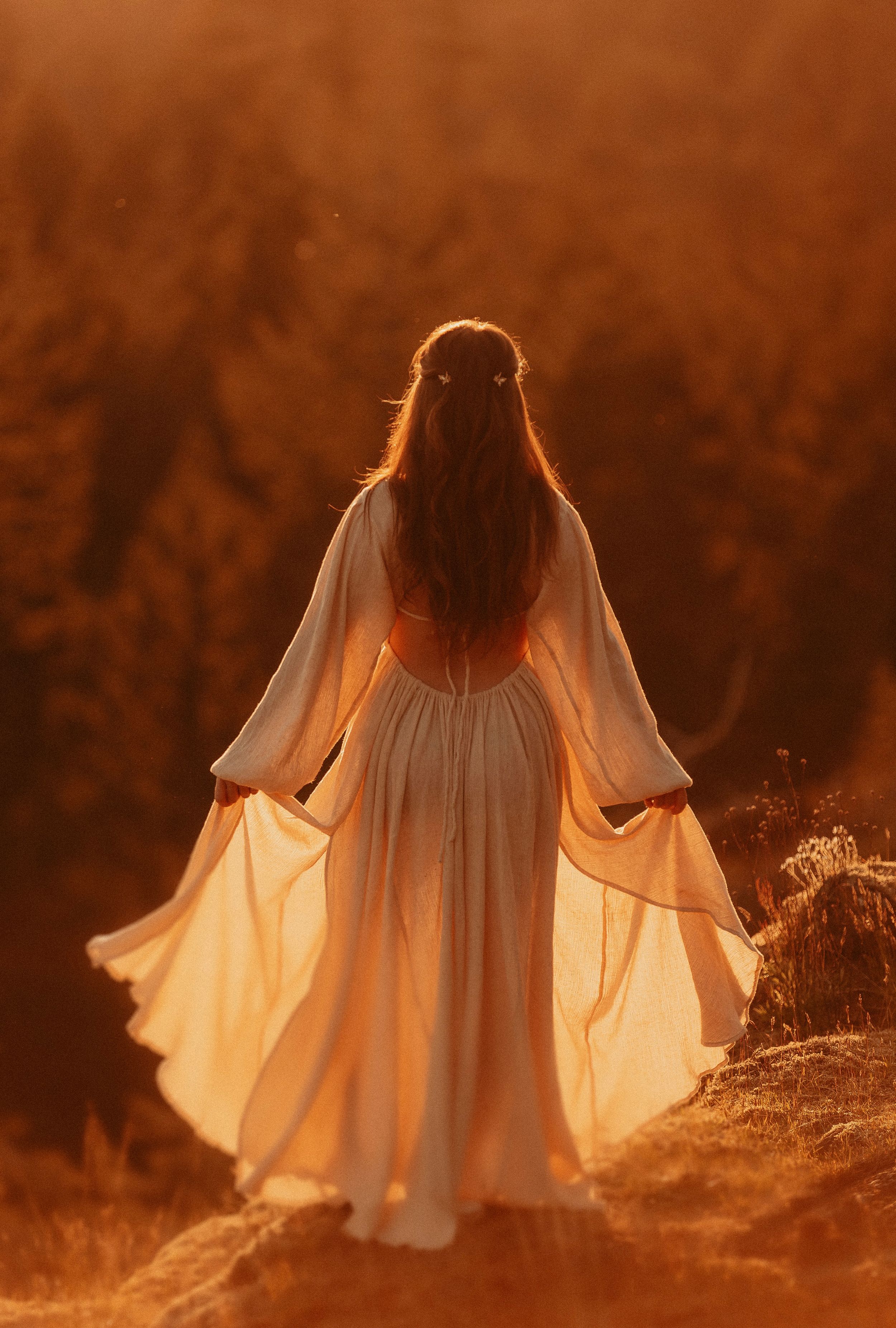 Silhouette of flowing white dress against warm sunset in tall grass.