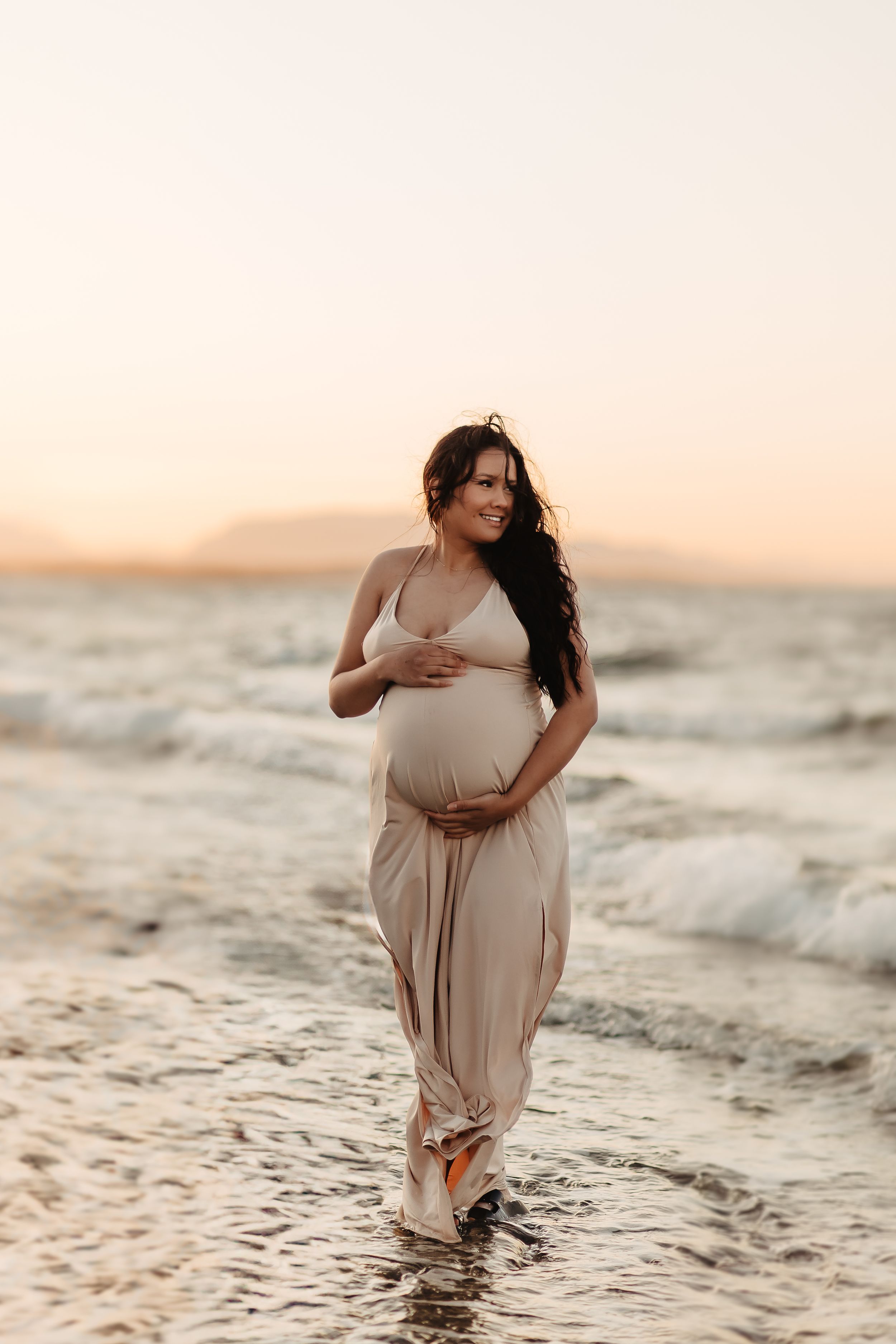 Maternity beach photoshoot at sunset with waves lapping at the shore.