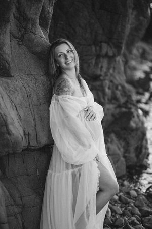 A person in a flowing white dress poses against a stone wall in a black and white portrait series.