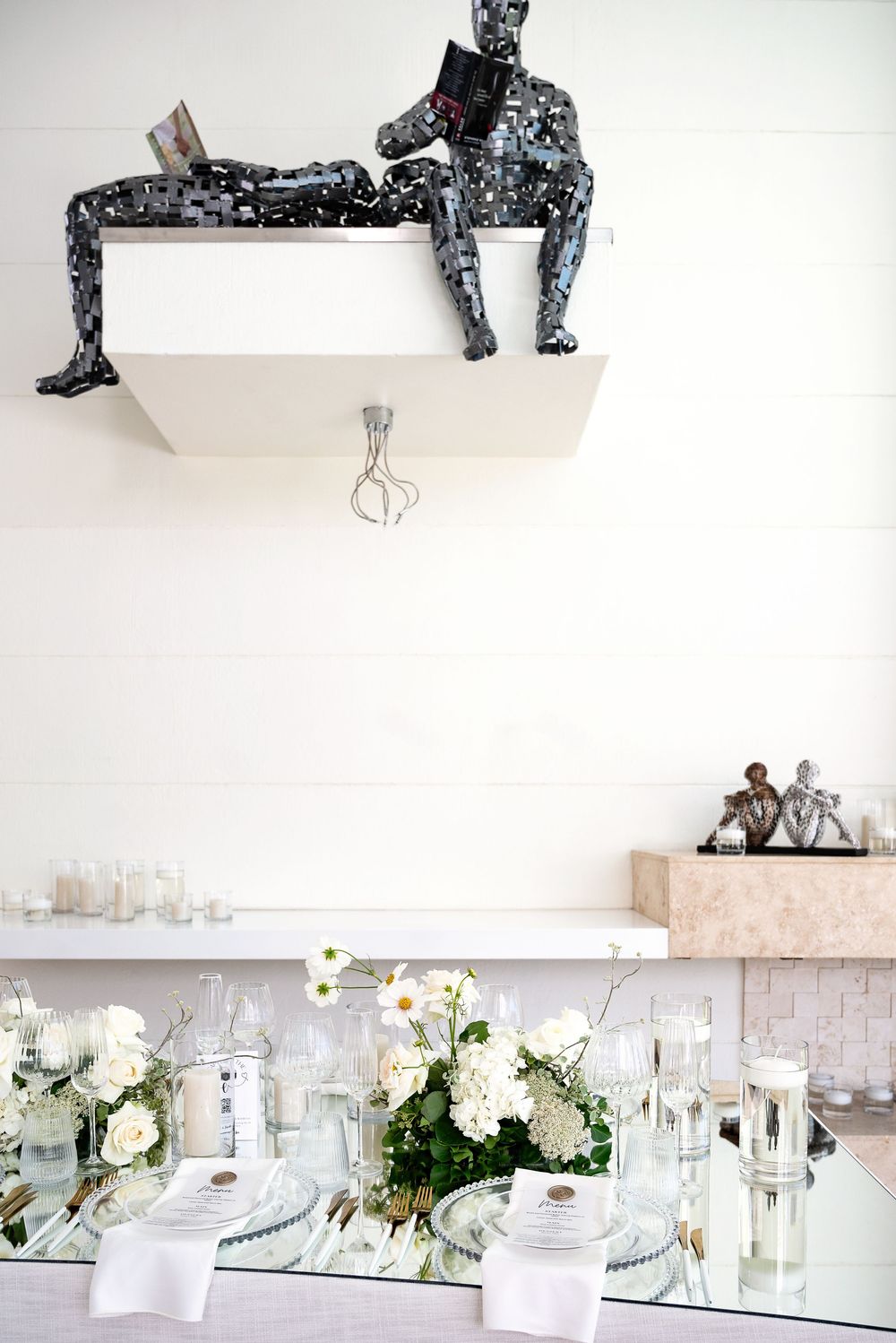 Elegant white floral table settings with glass candle holders and decorative lighting in a modern event space.