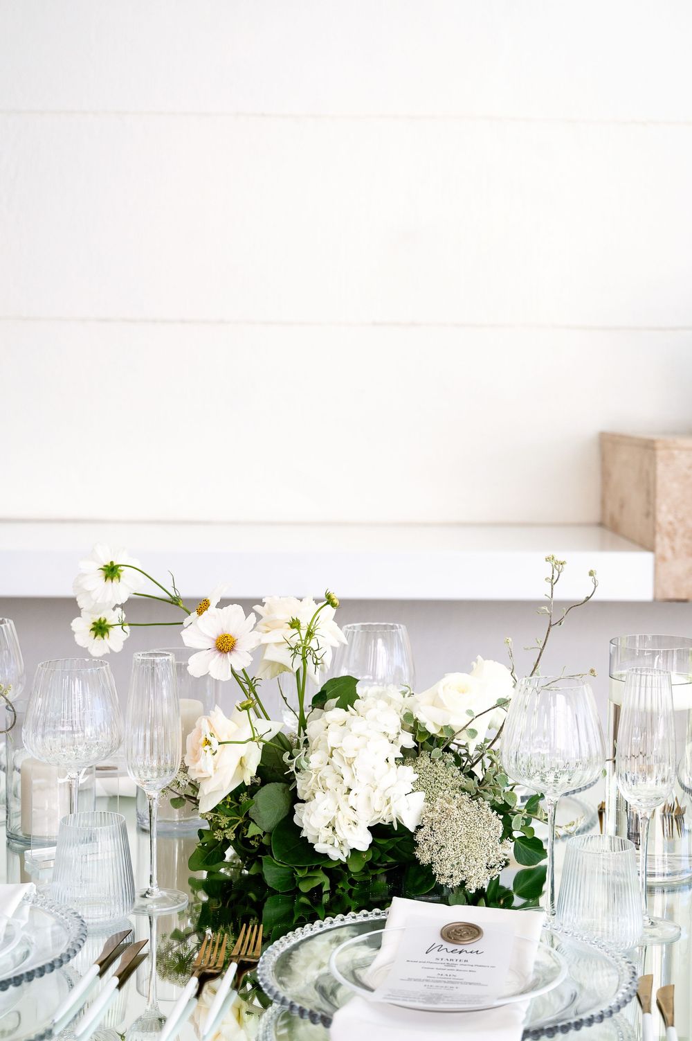 White floral table centerpieces with hydrangeas alongside elegant glassware at an upscale wedding reception.