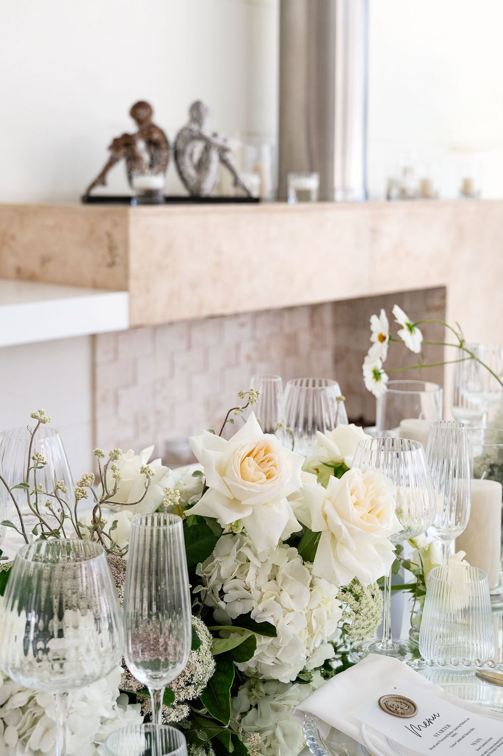 Elegant table setting with white floral centerpieces, crystal glassware and pale green accents for a wedding reception.