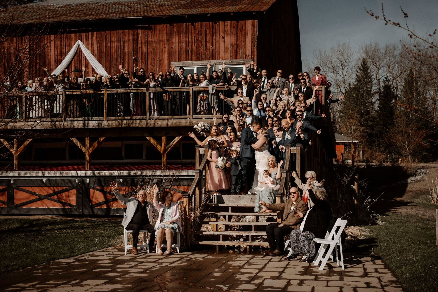 Wedding reception guests enjoy dinner in a rustic wood-beamed barn decorated with string lights and white linens.