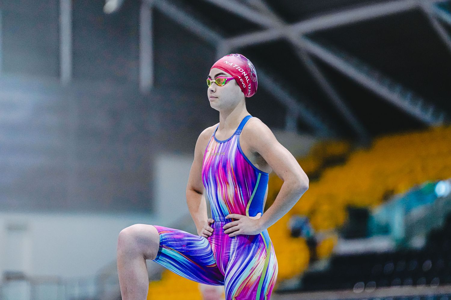 Competitive swimmers in navy swimsuits diving into the pool during a swimming competition event at an indoor facility.