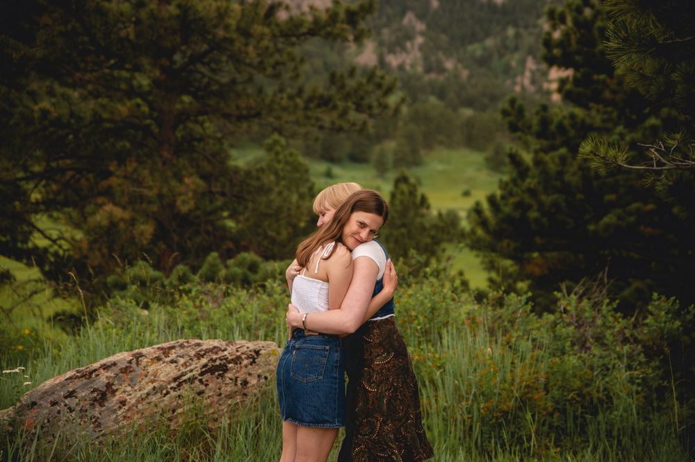 A romantic couple embraces during an outdoor photography session in a lush green mountain landscape at sunset.