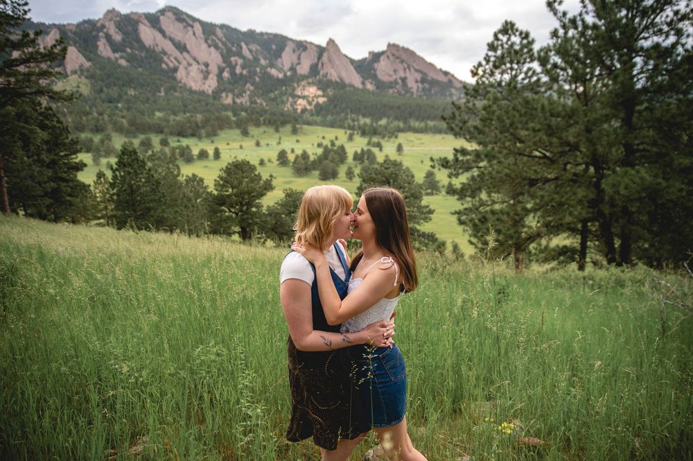 Two people embrace in a grassy meadow with the Flatirons rock formations of Boulder, Colorado in the background.