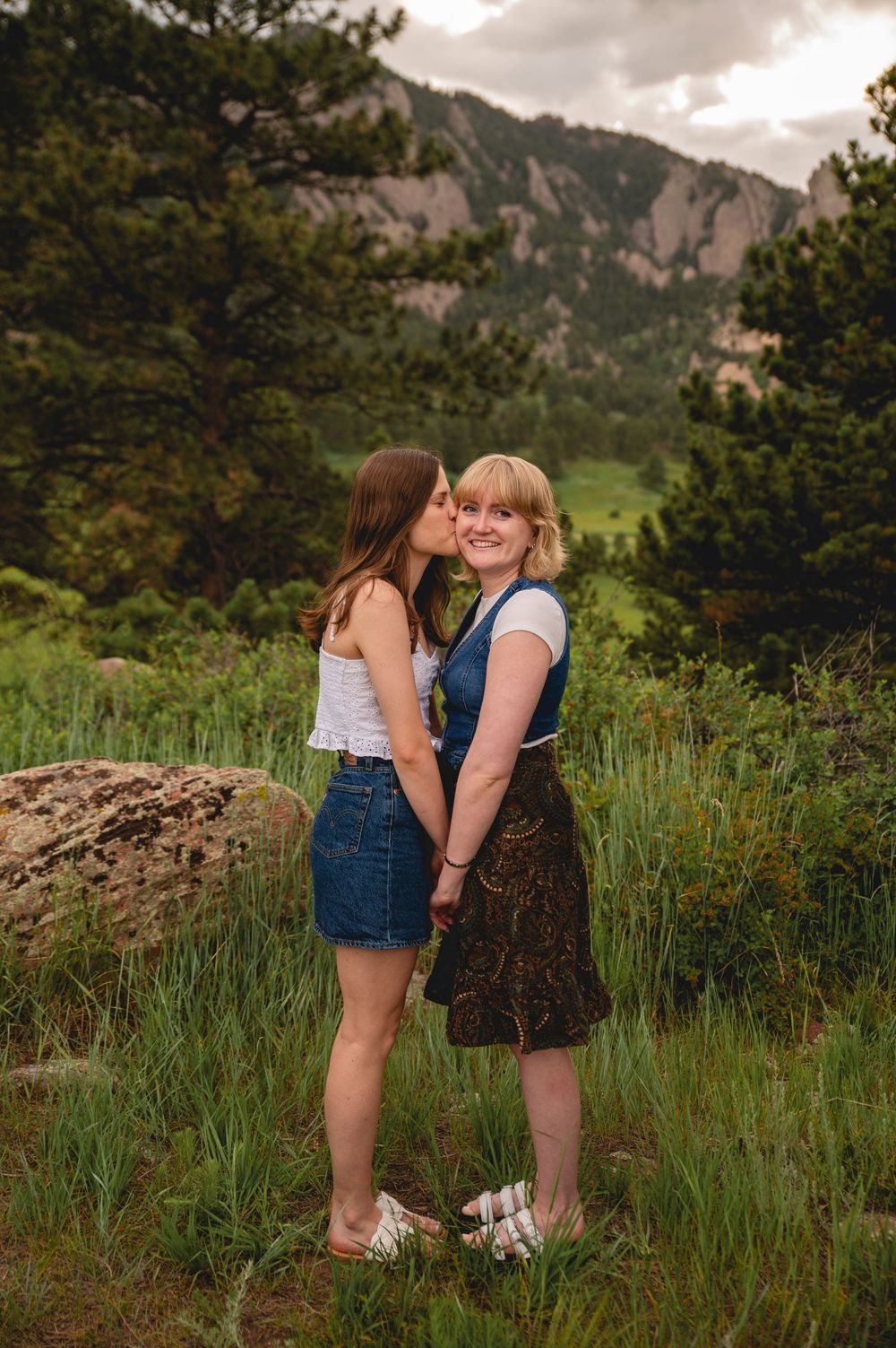 A romantic moment against a backdrop of mountain peaks and evergreen trees in a scenic outdoor setting during golden hour.