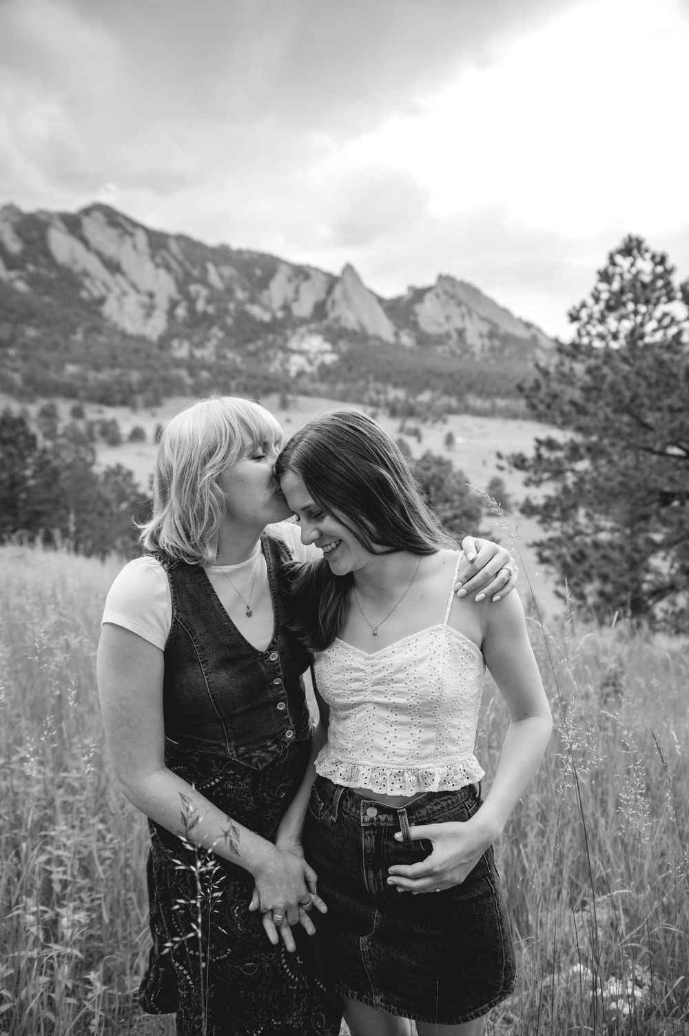 A tender moment shared between two people embracing in a field with dramatic mountain peaks rising in the background.