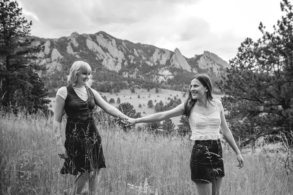 Two people dance and spin in a grassy field with dramatic mountain peaks rising in the background.