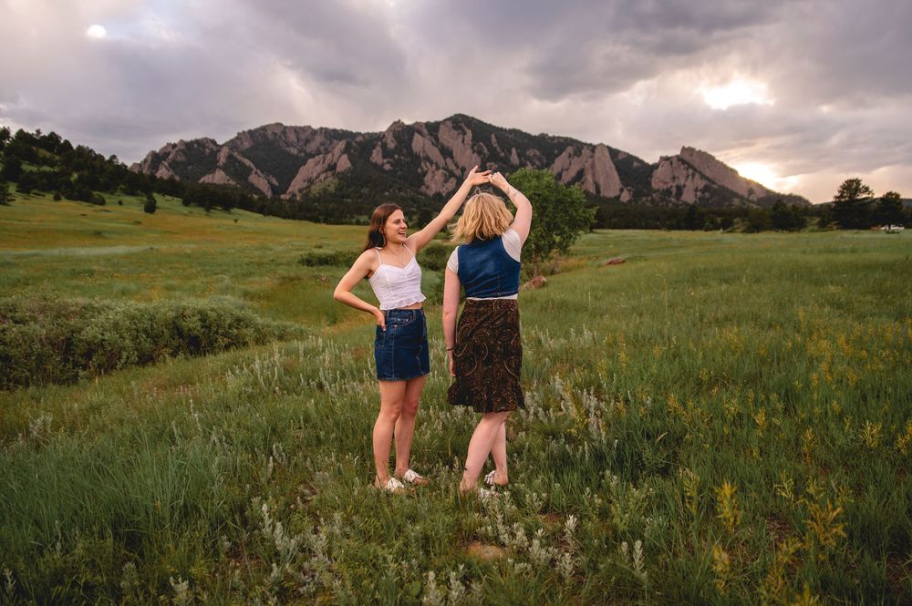 Two people dance in a grassy meadow at sunset with the Flatiron Mountains of Boulder, Colorado in the background.