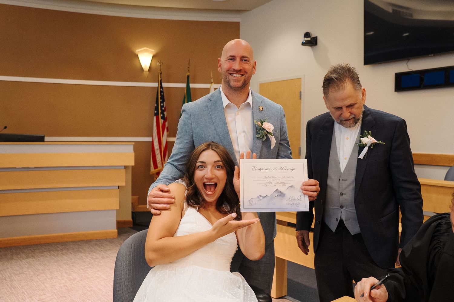A joyful wedding celebration moment in a courthouse room with three people showing a marriage certificate.