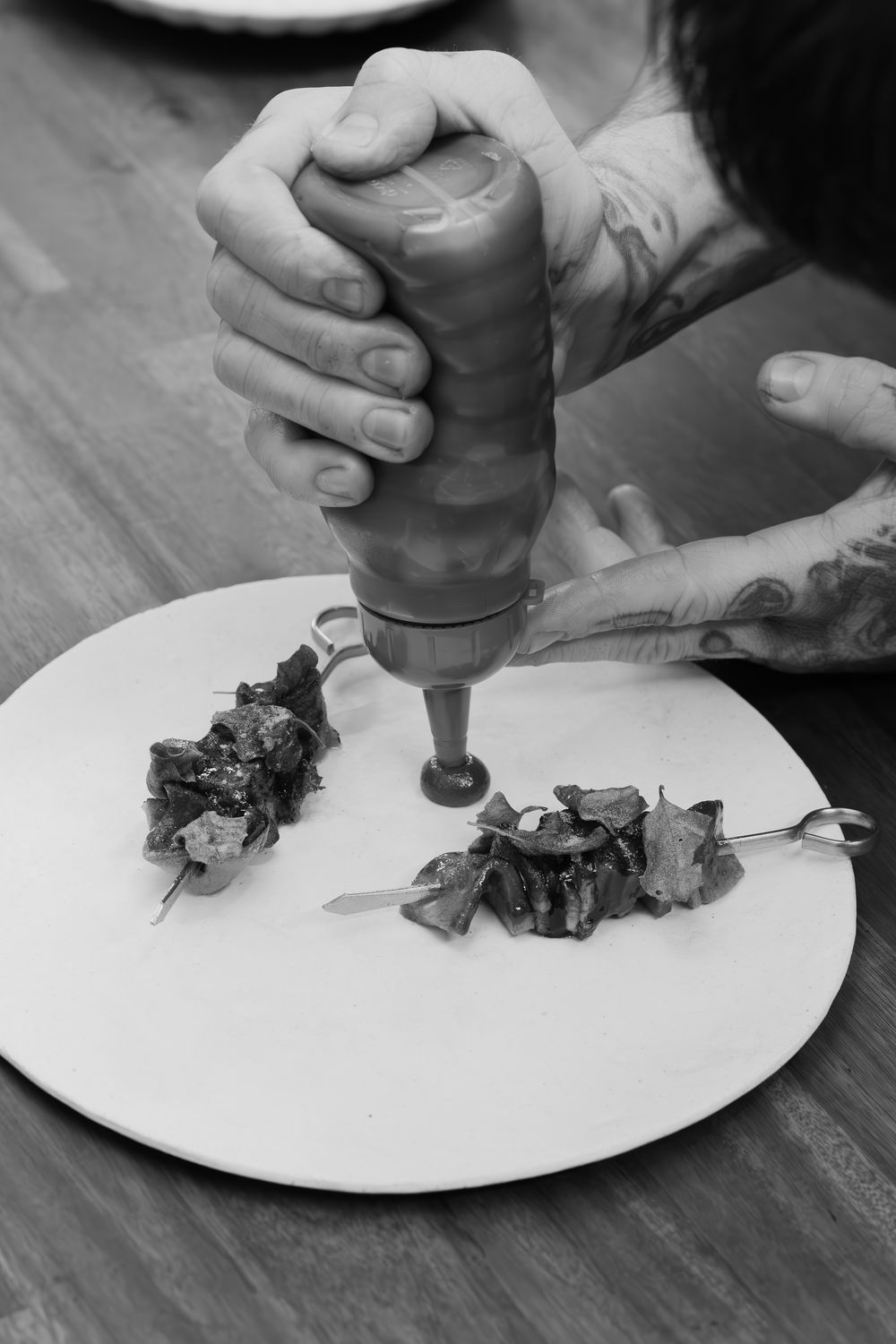 Hands using a pepper grinder to season food on a white plate in black and white photography.