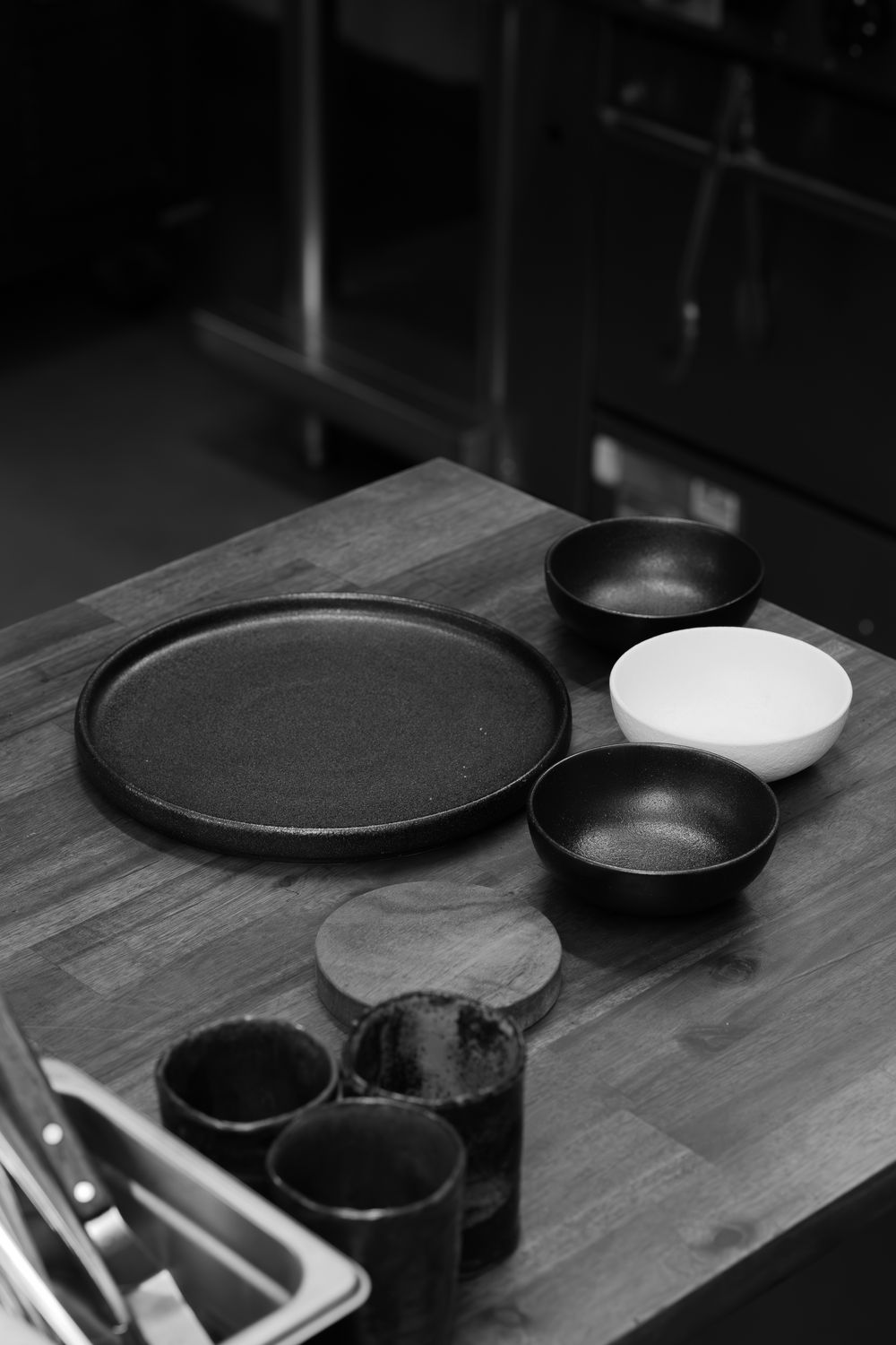 Black plates and white bowl arranged on a wooden table in a dark room.