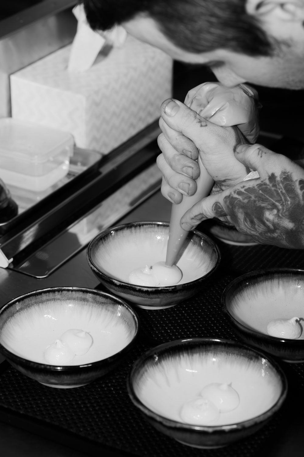 Hands preparing food on plates in a restaurant kitchen setting showing cooking process.
