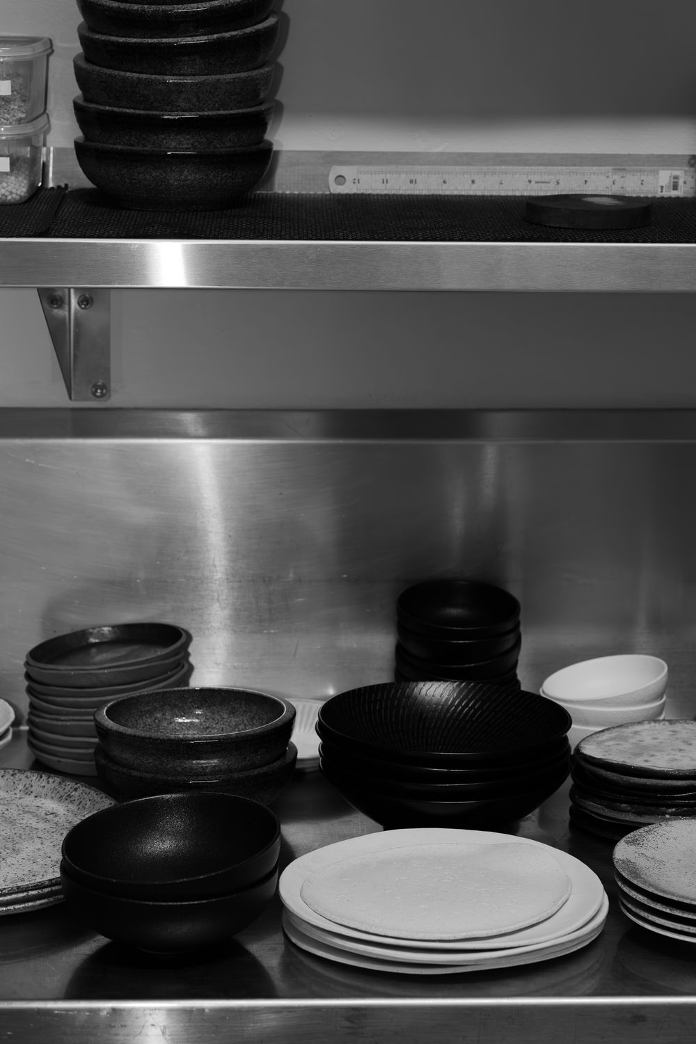 A collection of black and white restaurant plates and dishes stacked neatly on metal shelving in a commercial kitchen.