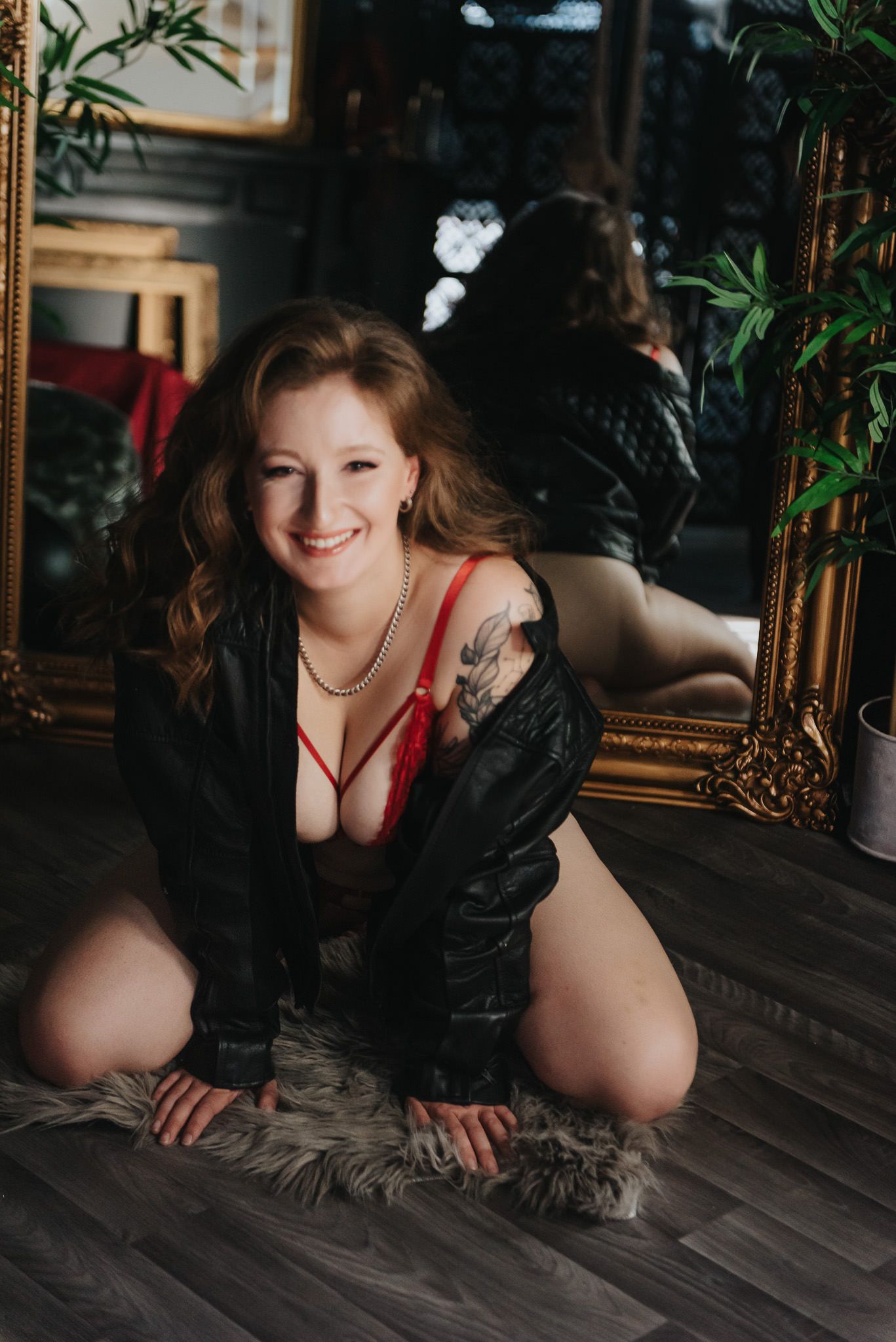 A boudoir photoshoot in a moody indoor setting with dark wood floors and ornate gold-framed mirrors.