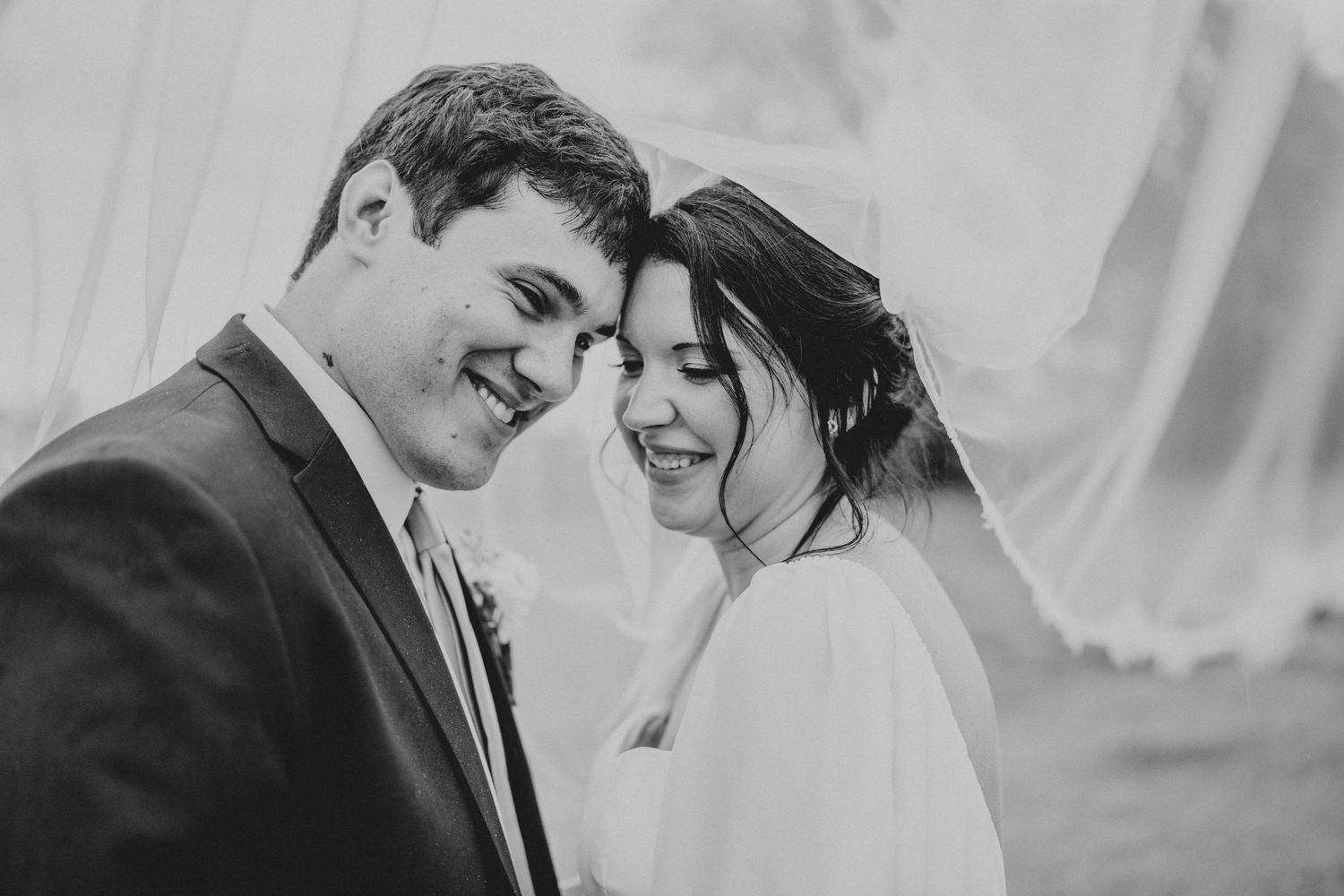Black and white wedding photo showing a happy couple sharing an intimate moment with soft smiles.