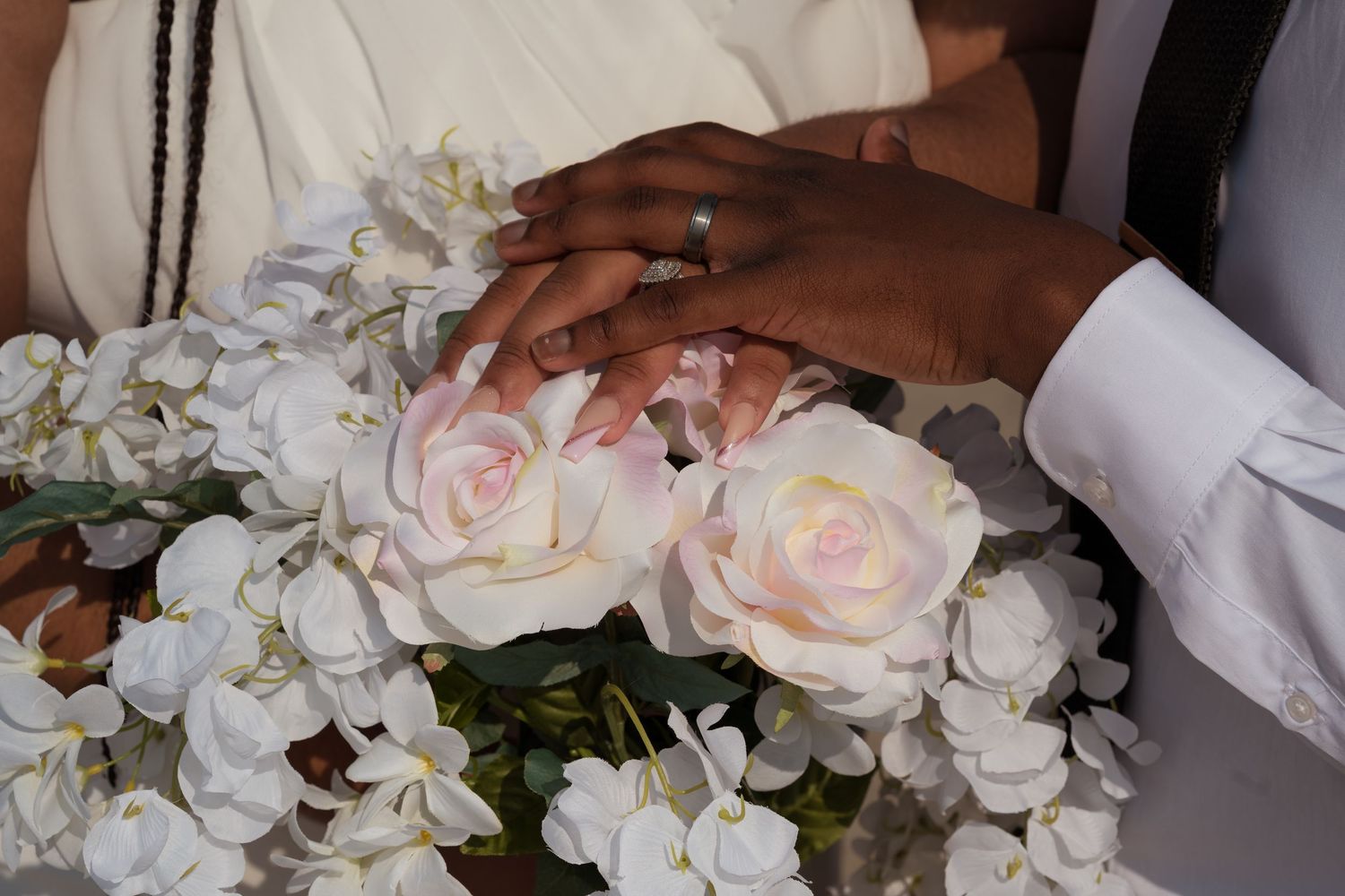 Hands holding a romantic wedding bouquet with soft pink roses and white orchids against a light background.