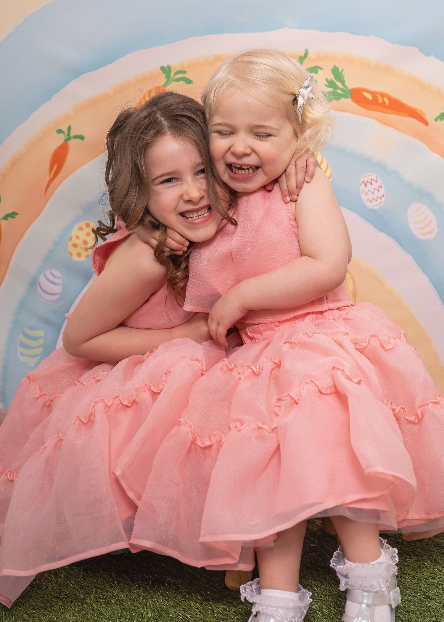 Easter Mini Session - Two children in pink dresses playing and laughing together on a colorful backdrop.