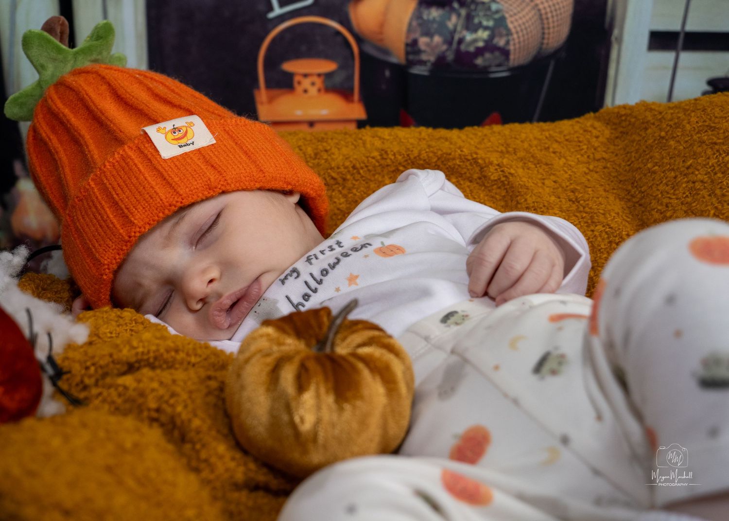 Sleeping baby surrounded by orange autumn decorations and pumpkins.