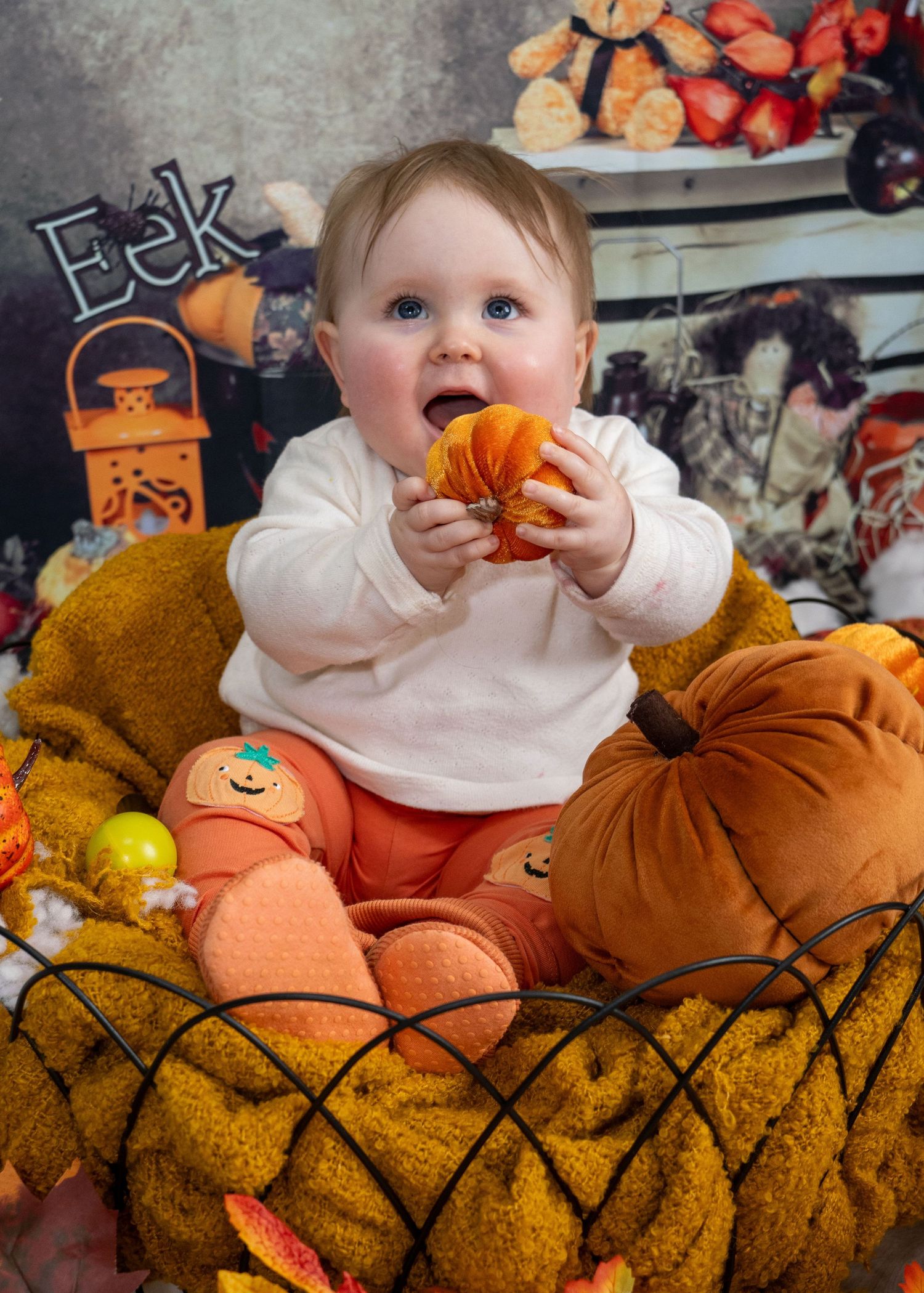 A seasonal photo featuring a baby playing with pumpkins on a yellow couch.