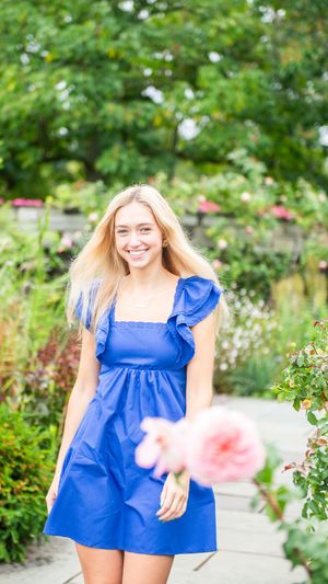 Person in royal blue summer dress standing in garden with blooming flowers.