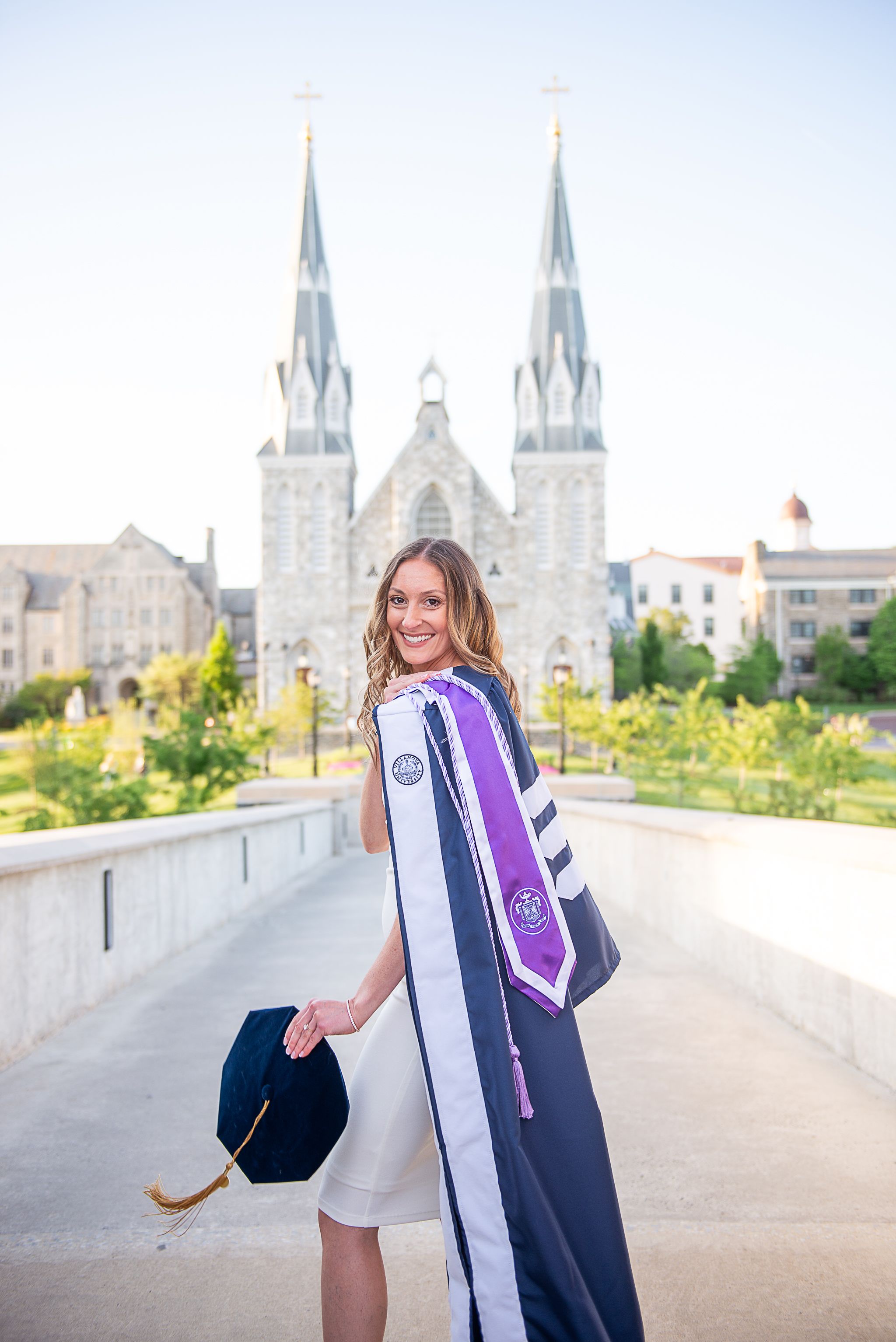 Graduate in cap and gown poses in front of cathedral spires during commencement celebration at Villanova University.