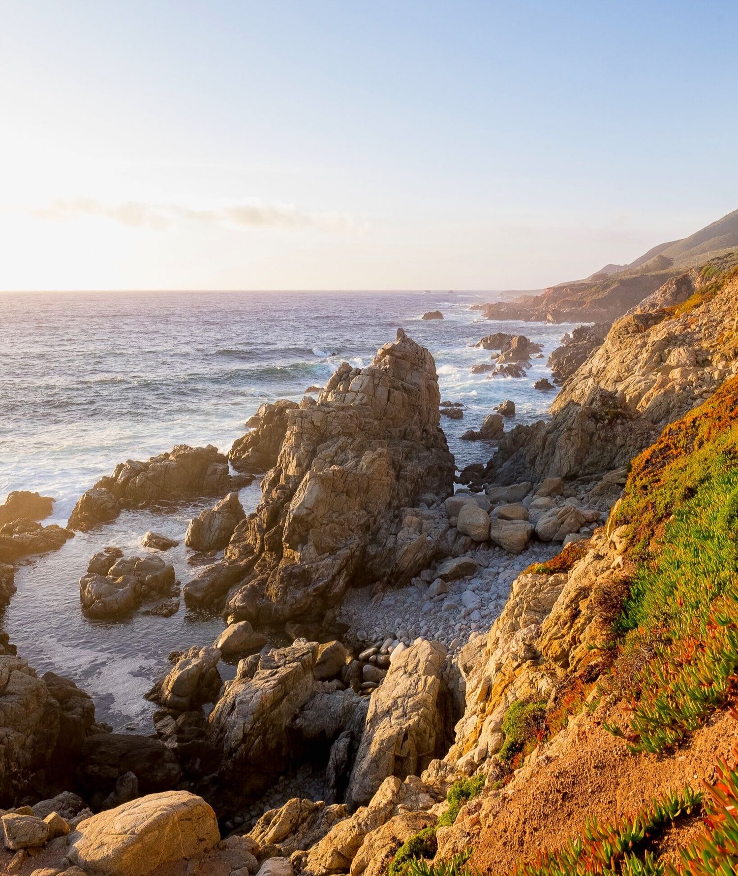 Rocky coastal landscape at golden hour with waves crashing against cliffs.