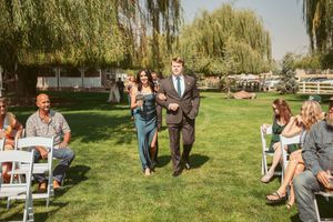 Outdoor wedding seating arranged on a lush lawn with white folding chairs under a shady tree.