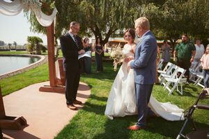 An outdoor wedding ceremony takes place on a grassy lawn next to a lake with chairs set up for guests.