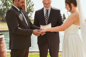 Wedding couple exchanging vows in front of officiant during outdoor garden ceremony.