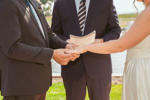 Close up of couple holding hands during wedding ceremony with officiant in background.