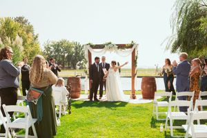 Outdoor wedding guests seated in white chairs on green grass with natural scenery in background.