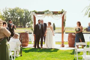 Outdoor garden wedding with wooden arch, white draping and wine barrels as decor.