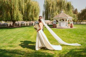 Wedding dress with flowing train in garden setting with white gazebo in background.