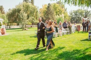 Wedding guests seated on chairs arranged outdoors under weeping willow trees for an intimate ceremony.