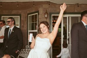 Joyful guest raises their arm in celebration while holding a drink at an outdoor wedding reception.