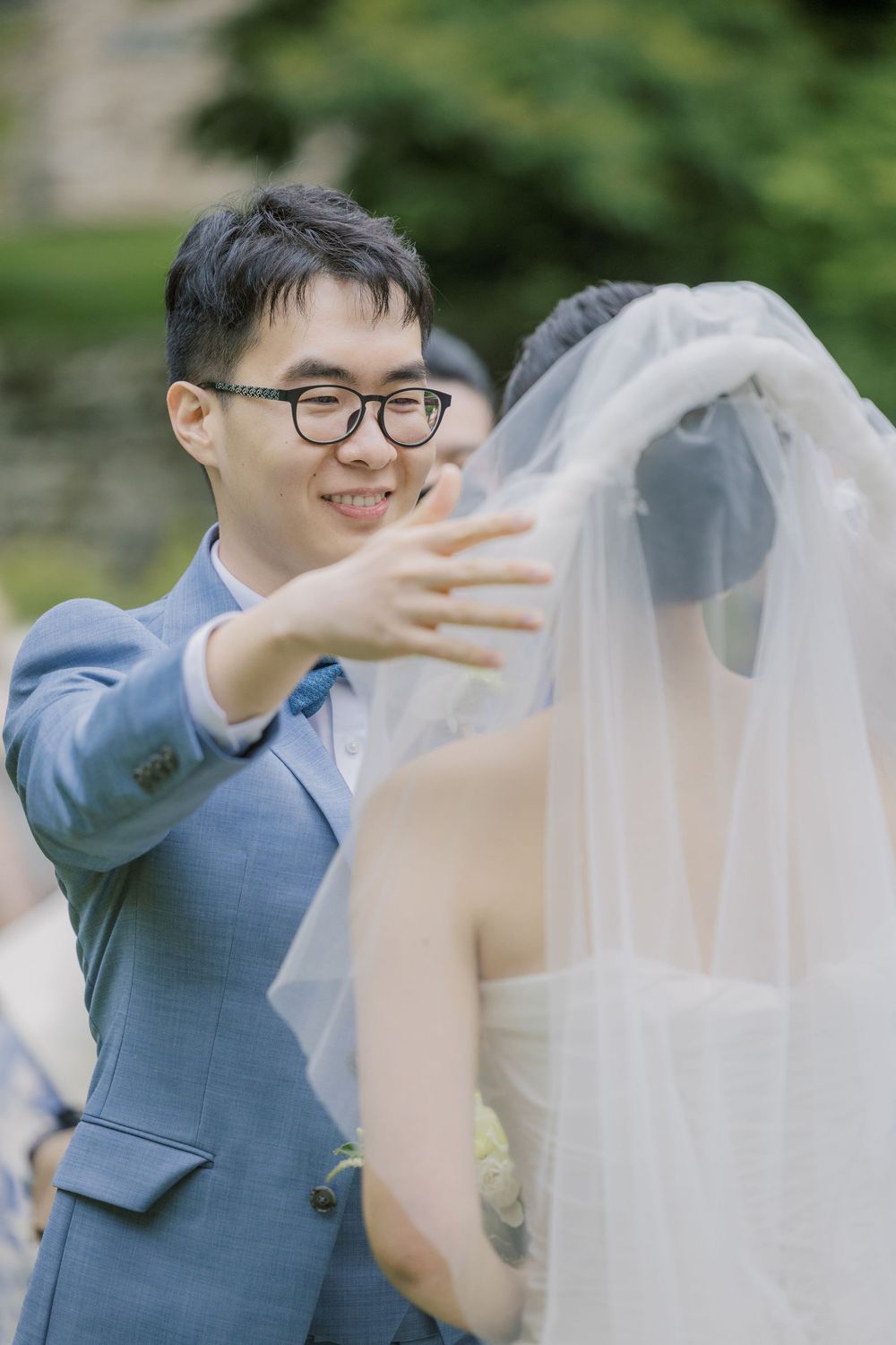 A tender moment between newlyweds as the groom lifts his bride's veil in an outdoor garden setting.