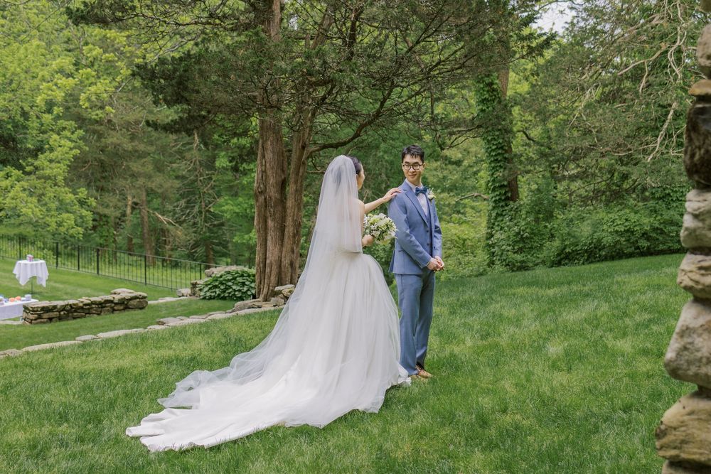 Couple poses for wedding photos on green lawn with bride's dramatic train on display.