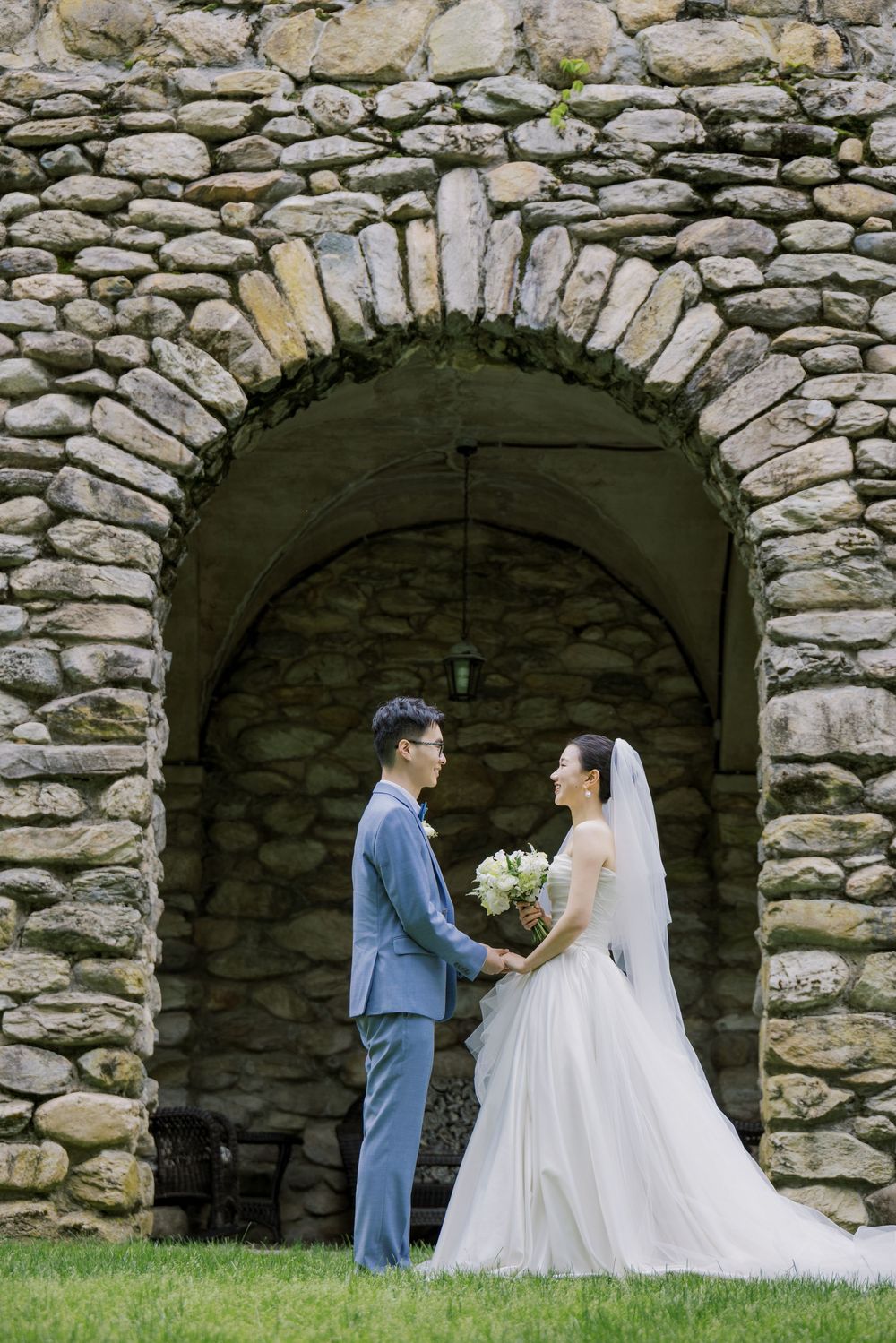 A wedding couple poses for photos under a rustic stone archway during their romantic outdoor ceremony.
