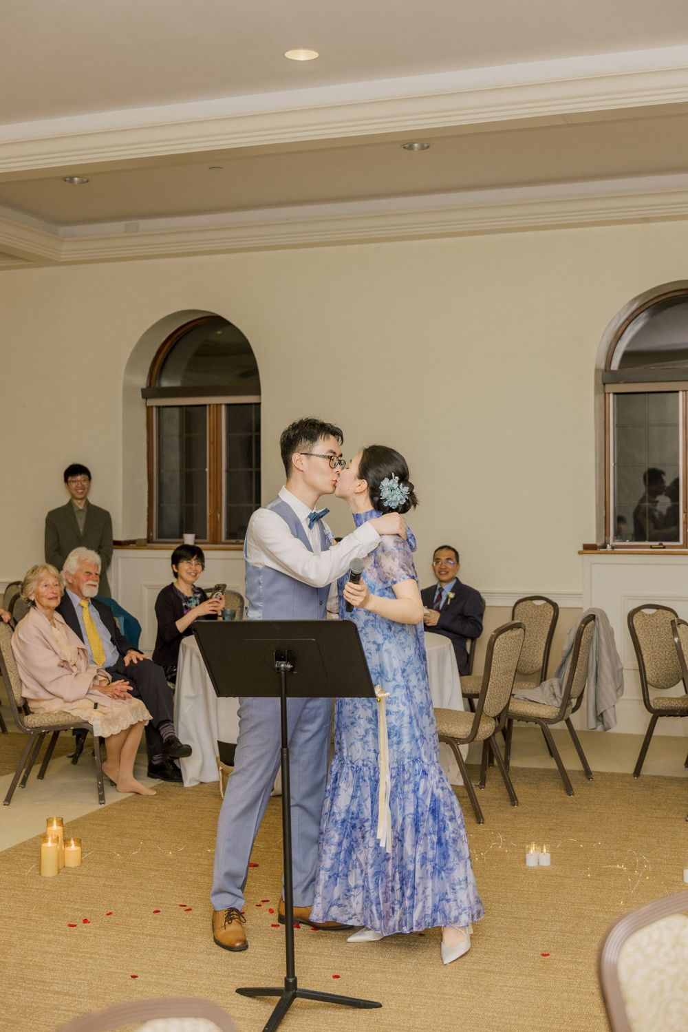 A couple performs a duet together at their wedding reception with guests seated in the background.
