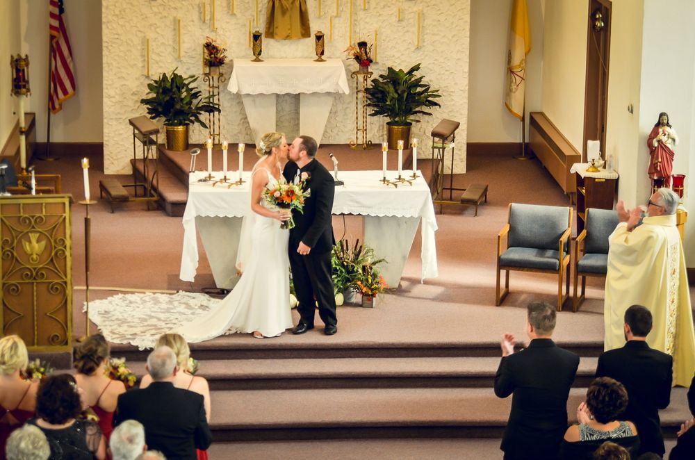 A traditional church wedding ceremony taking place in a sanctuary with white floral arrangements and candles at the altar.