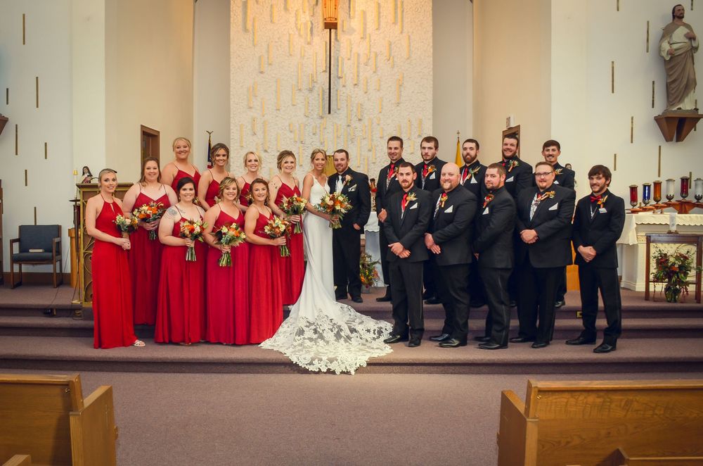 A wedding party in a church with bridesmaids in red dresses and groomsmen in black suits standing at the altar.
